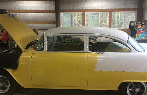 A classic yellow car with the hood open. The car is parked in a garage.