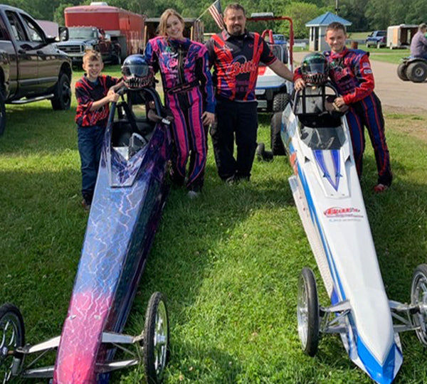 A family of racers stands proudly by two racing vehicles.